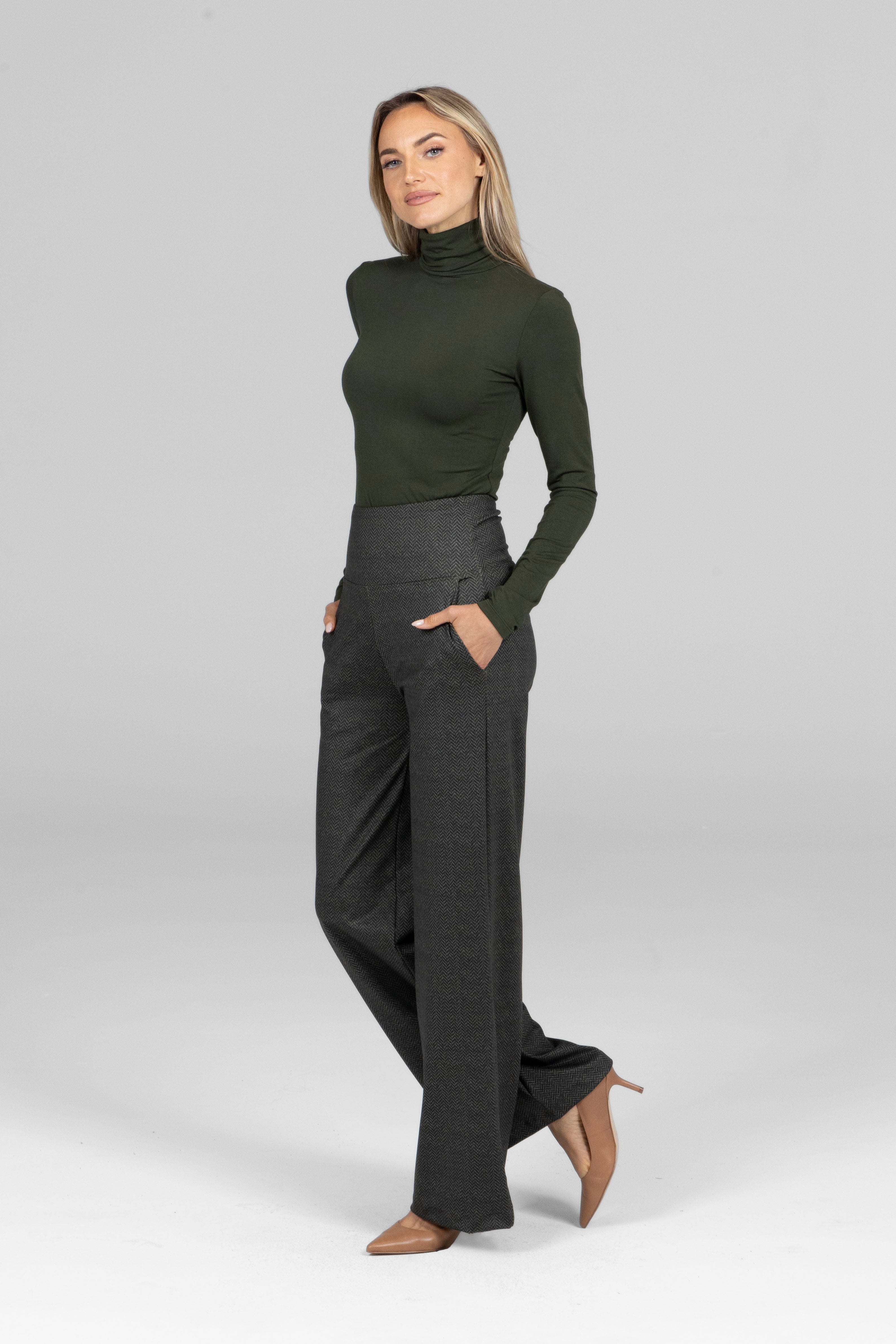 Woman wearing a green turtleneck and gray pants on a white background