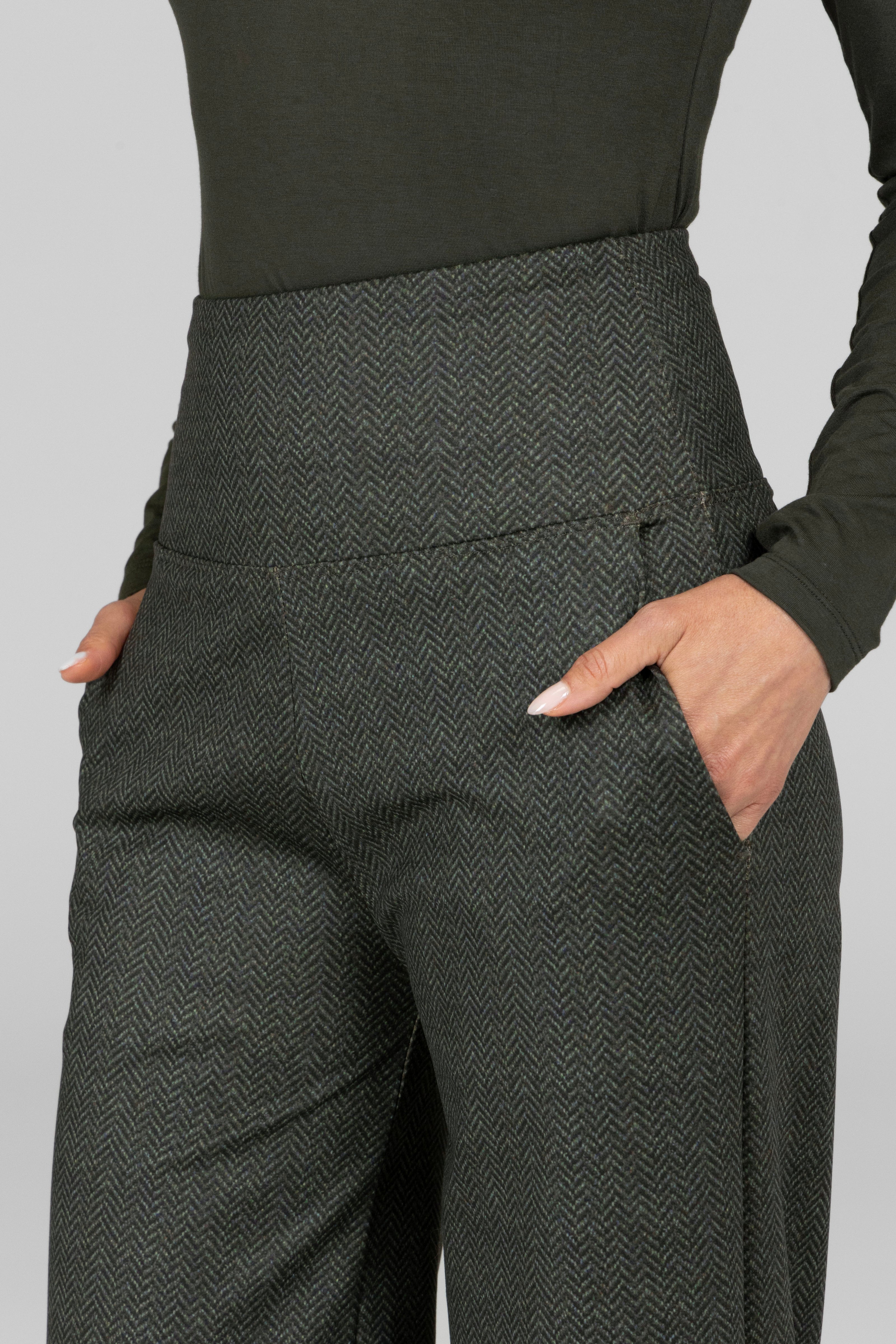 Dark gray herringbone pants worn with a black top on a light gray background