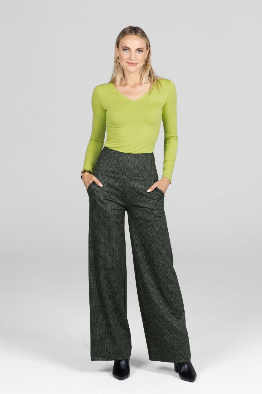 Woman wearing a green top and dark green wide-leg pants on a white background