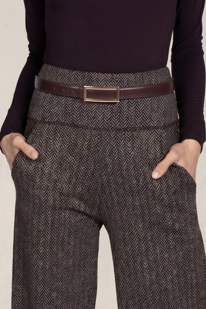 Person wearing a dark long-sleeve top and brown herringbone pants with a brown belt.