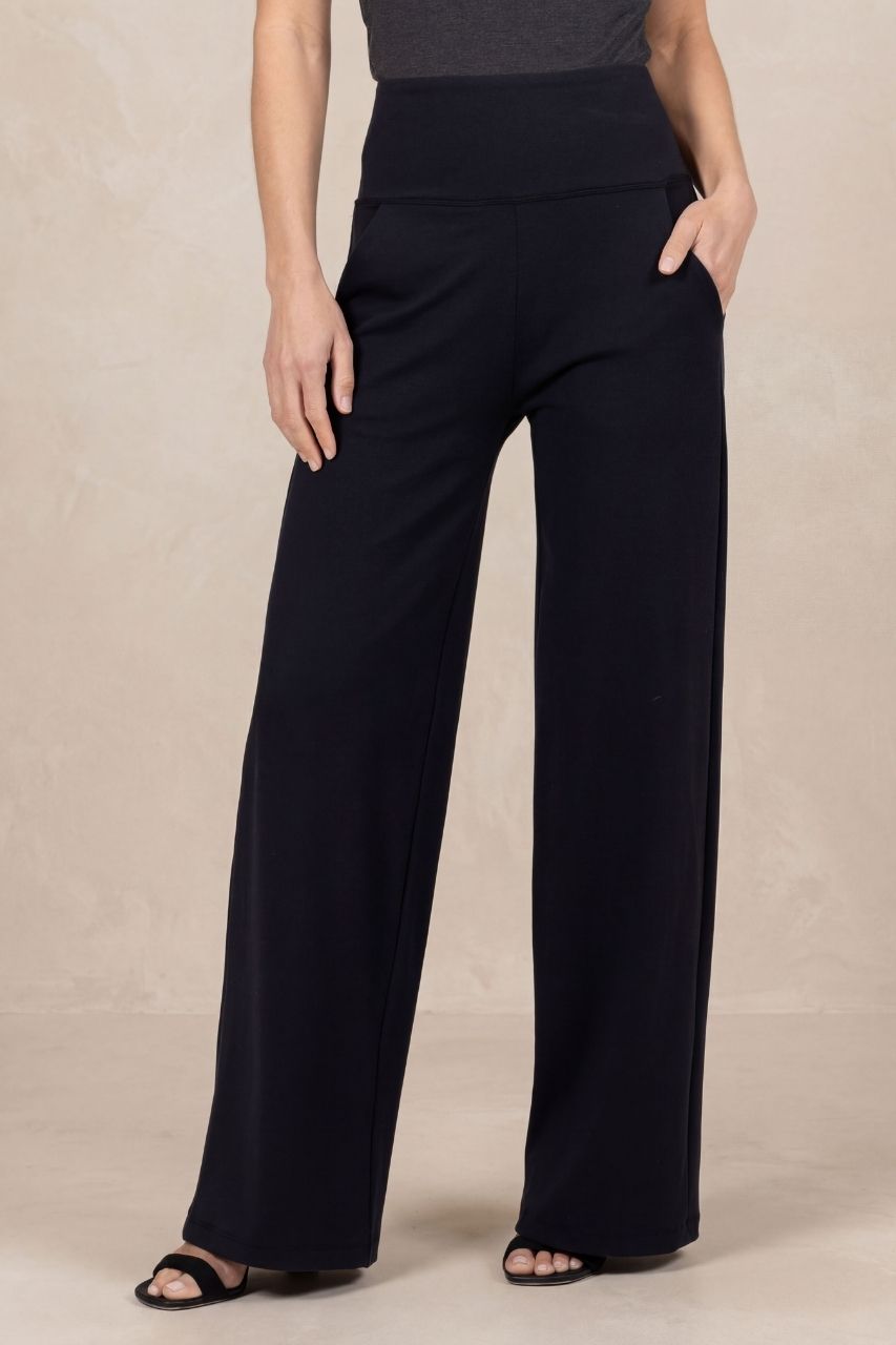 Model wearing black high waist wide leg pants in front of a beige background