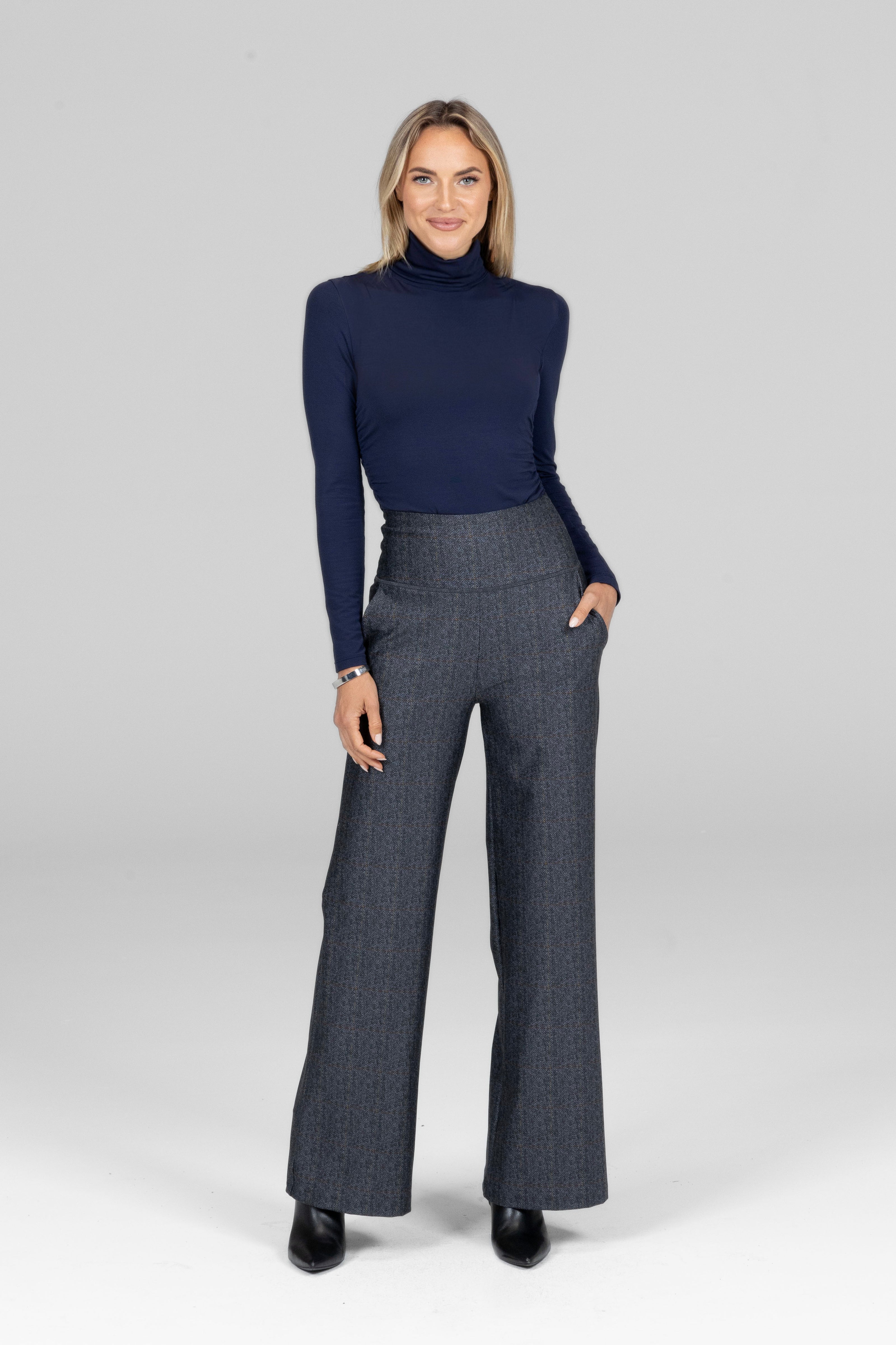 Woman wearing a navy turtleneck and gray high waist wide leg pants on a white background