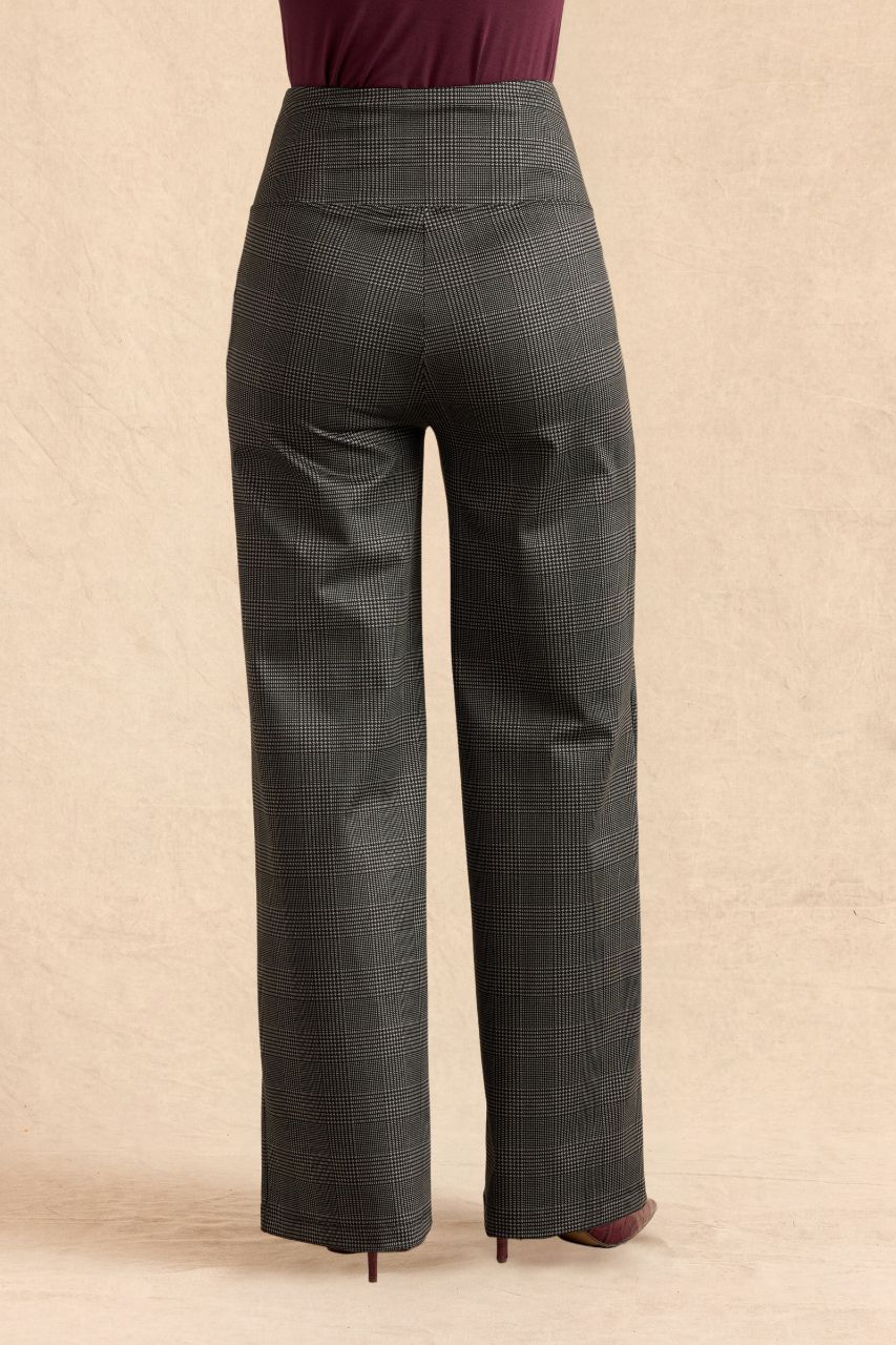 A pair of high-waisted, wide-leg trousers in a dark gray and black windowpane plaid pattern, shown from the back on a model wearing a burgundy top and heels, against a textured beige backdrop.