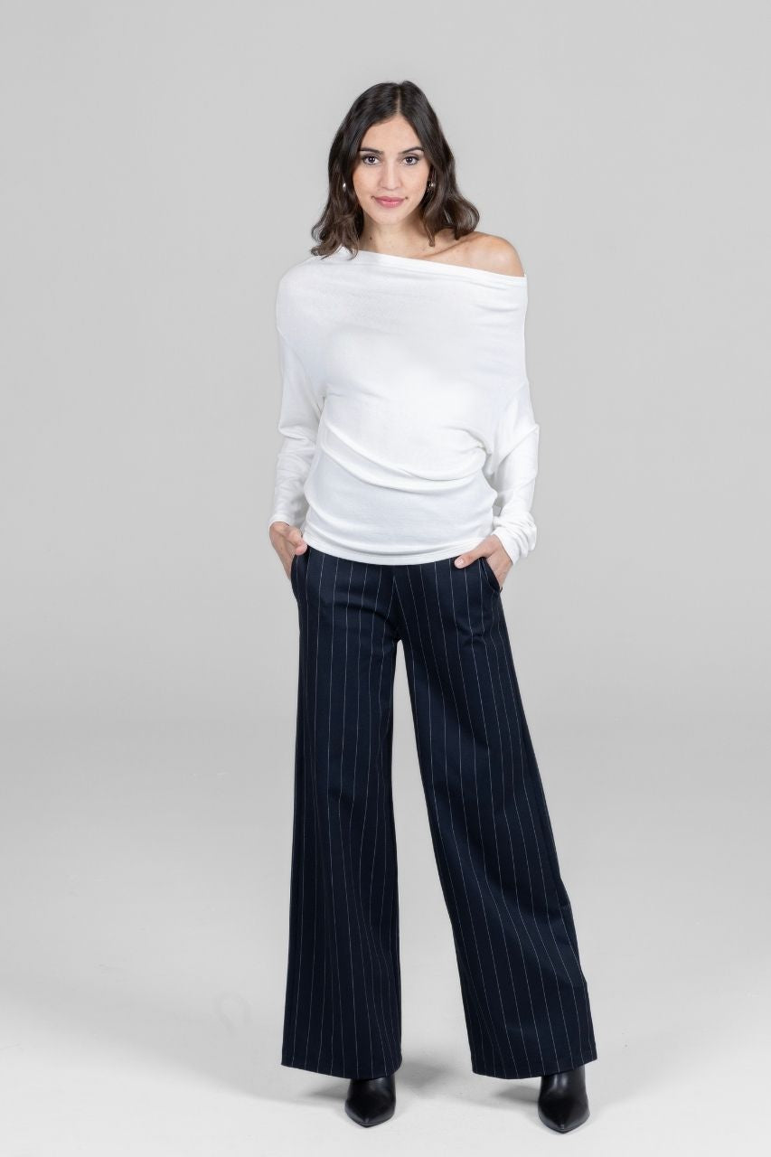 Woman wearing a white off-shoulder sweater and black pinstripe wide leg pants on a gray background