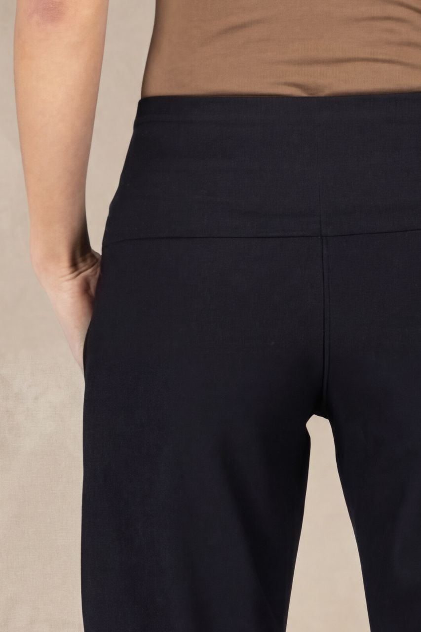 Close up view of black pants worn by a person on a beige background