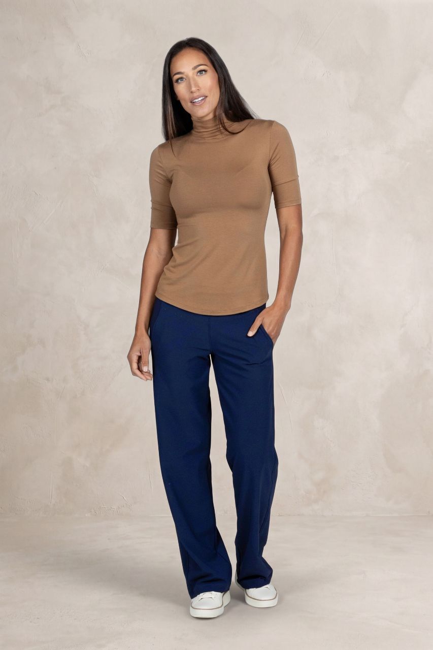 Woman wearing a brown mock neck and blue pants against a beige background