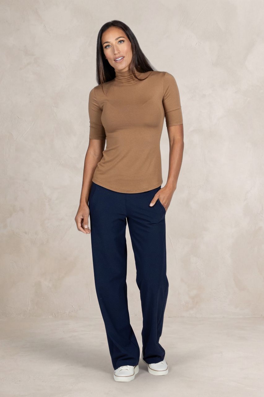 Woman wearing a brown top and navy pants against a beige background