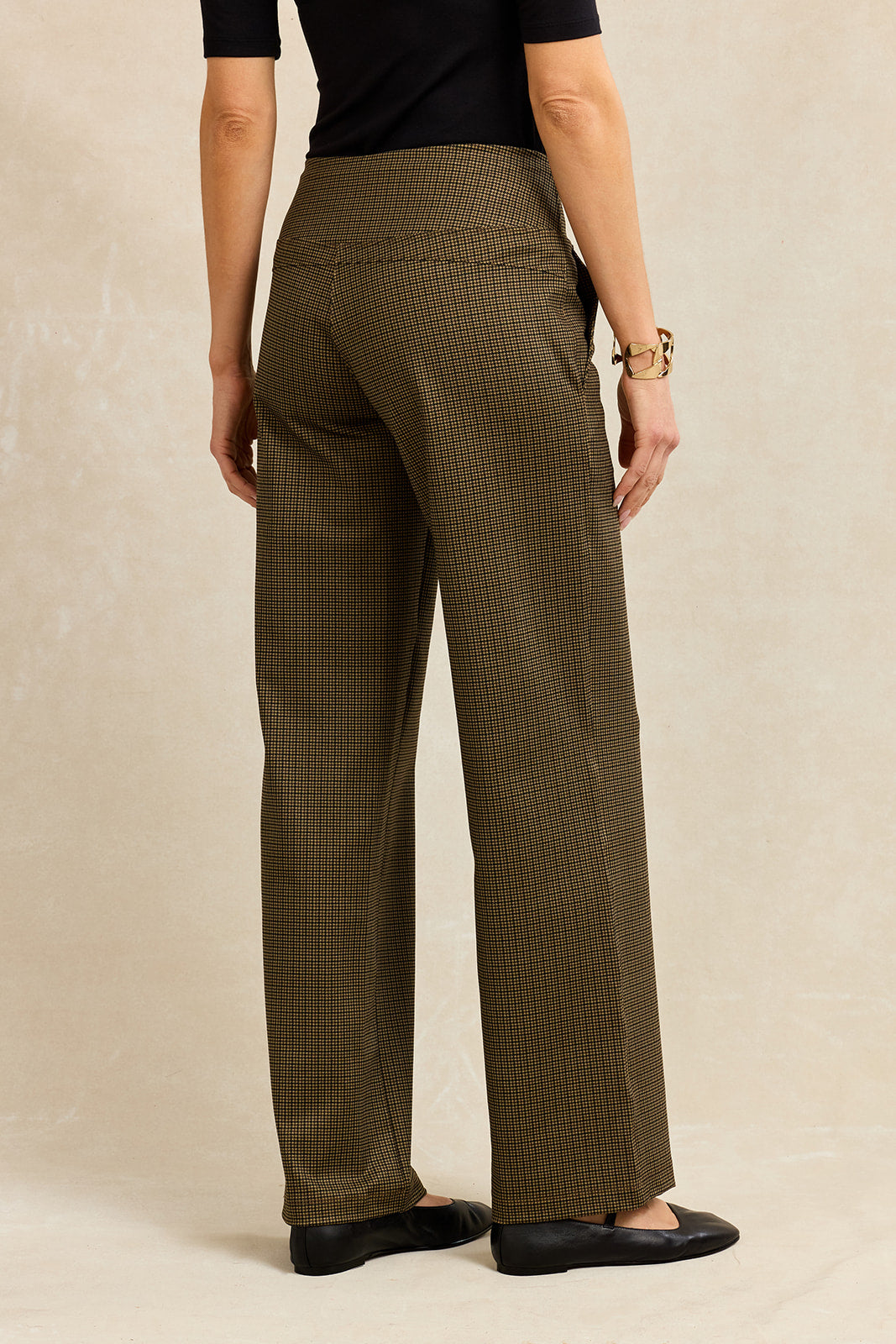 Back view of a person wearing brown houndstooth pants on a beige background