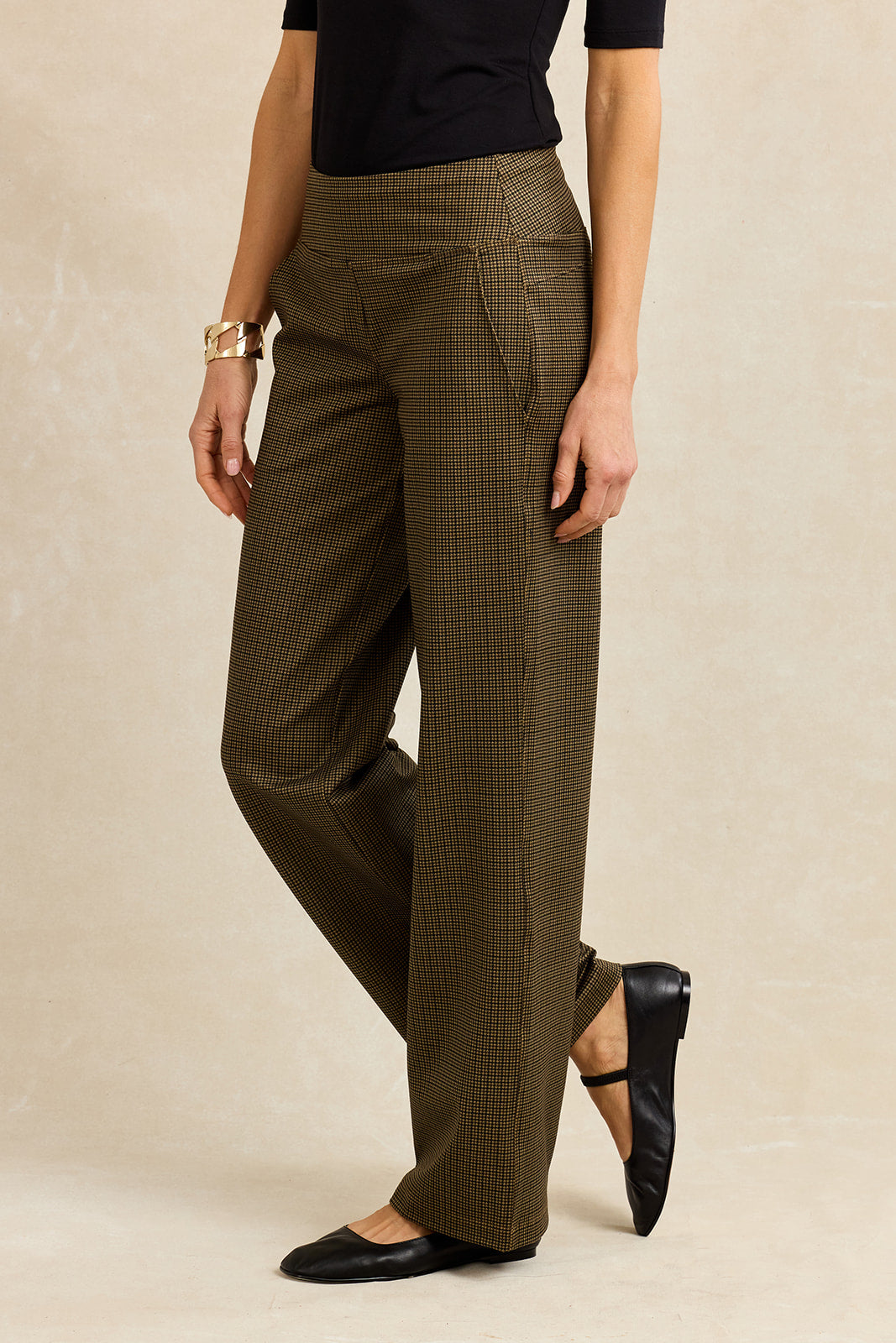 Person wearing brown houndstooth pants on a beige background mid step