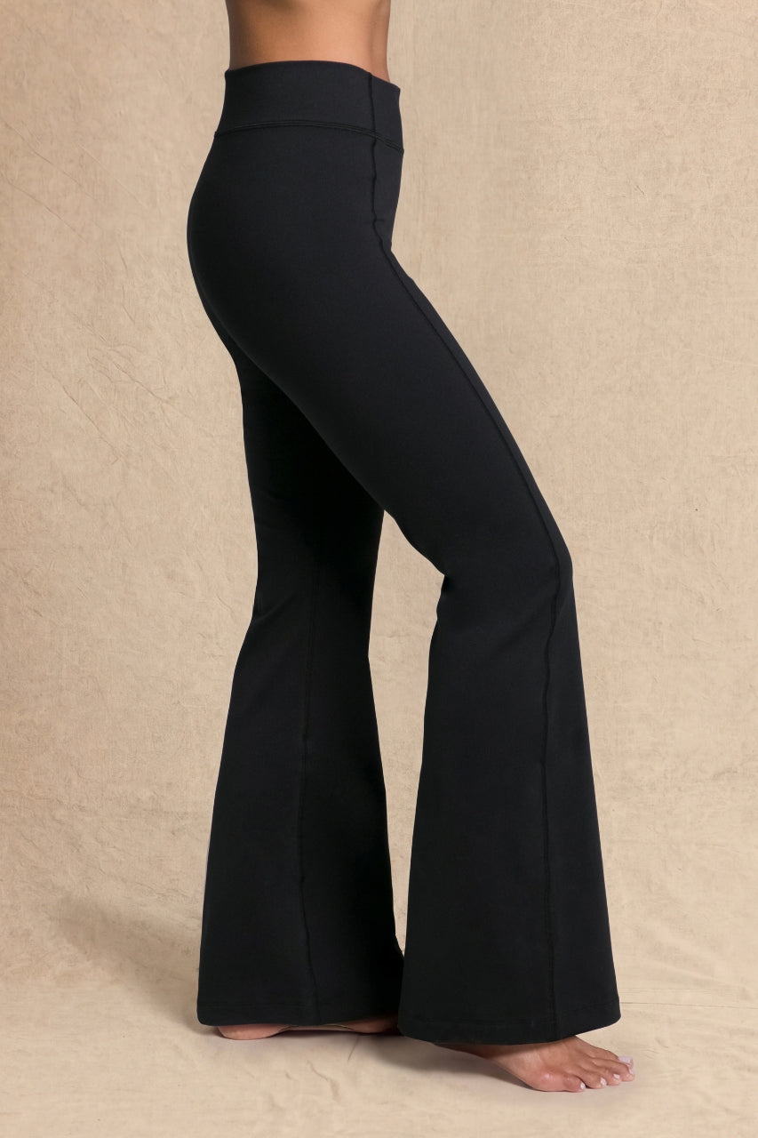 Black high-waisted flared pants shown on a model from the waist down, standing barefoot against a textured beige backdrop.