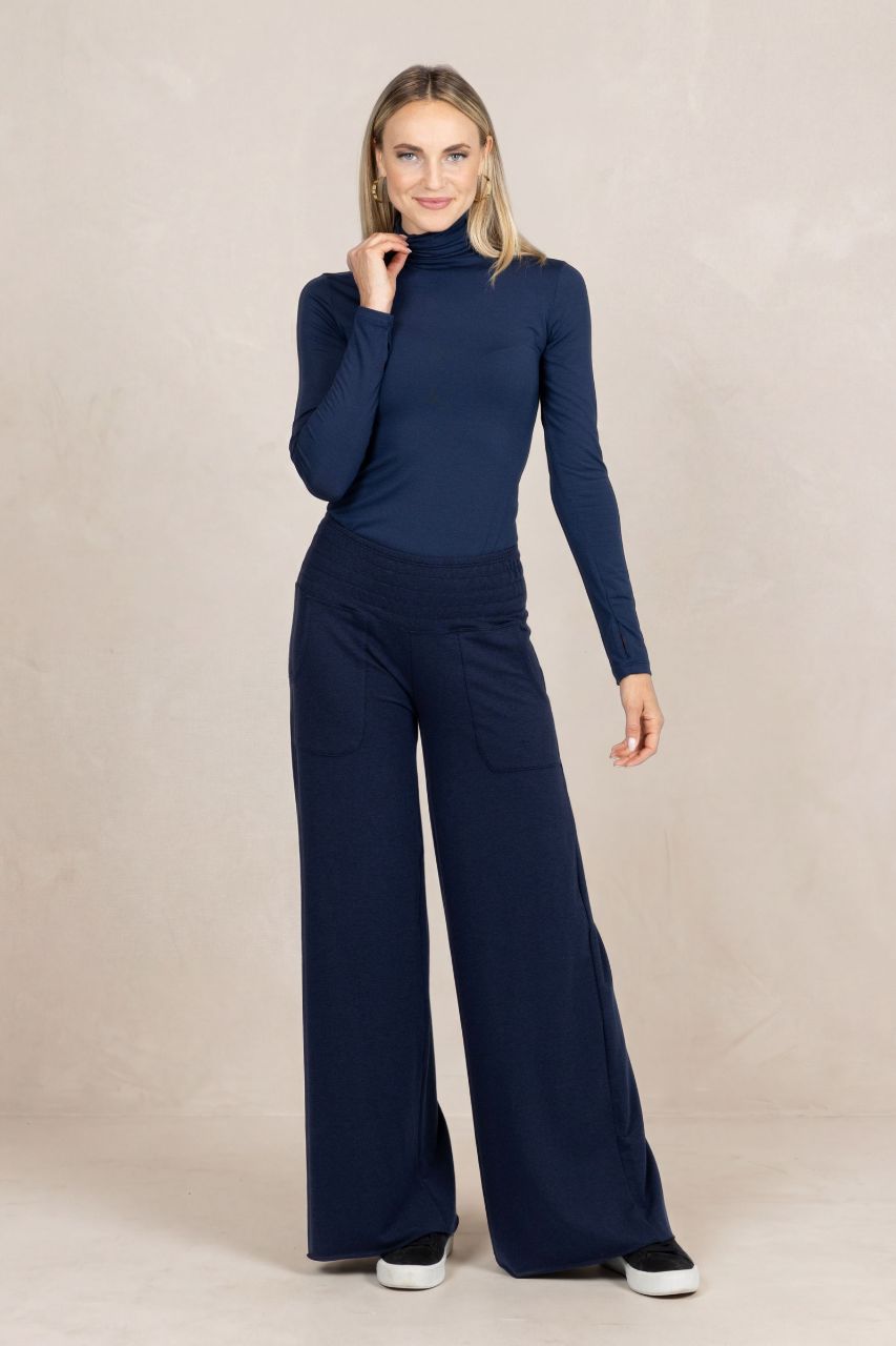 Woman wearing a navy blue turtleneck and wide-leg pants on a beige background