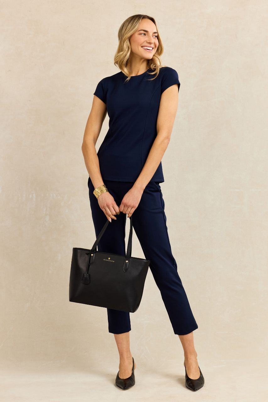 Woman in navy outfit holding a black tote bag against a beige background