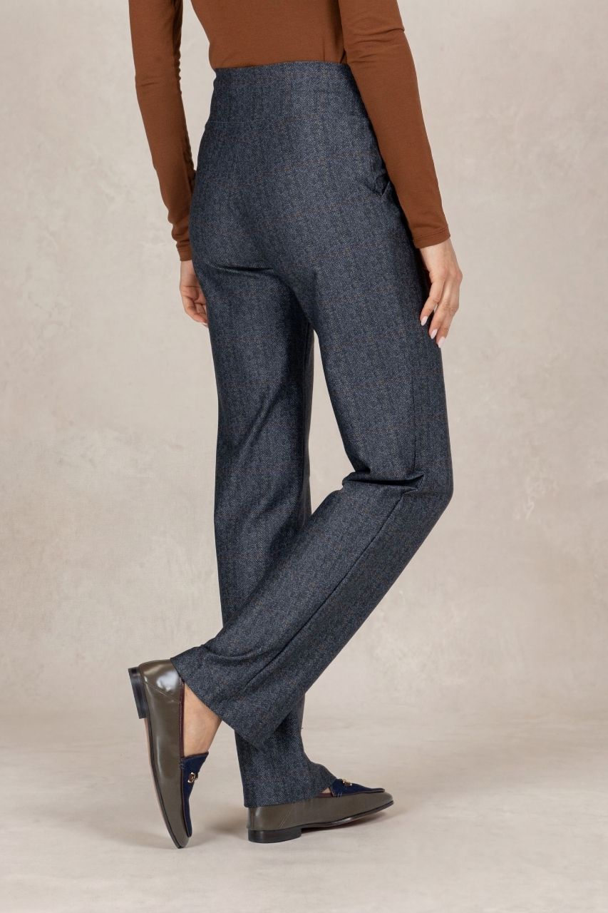 Back view of a woman wearing grey tartan straight leg pants on a beige background