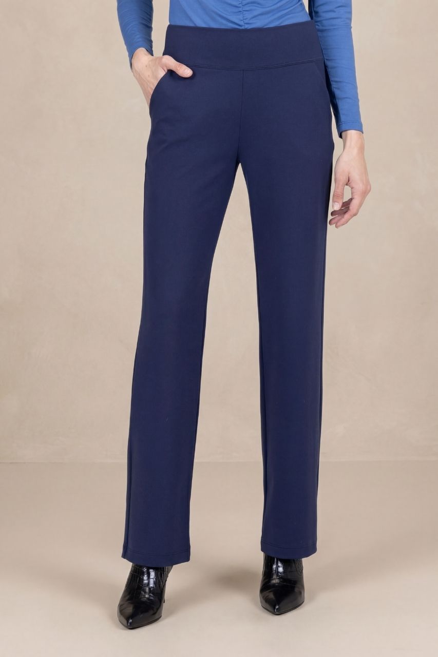 Woman wearing navy blue straight leg pants in front of a beige background