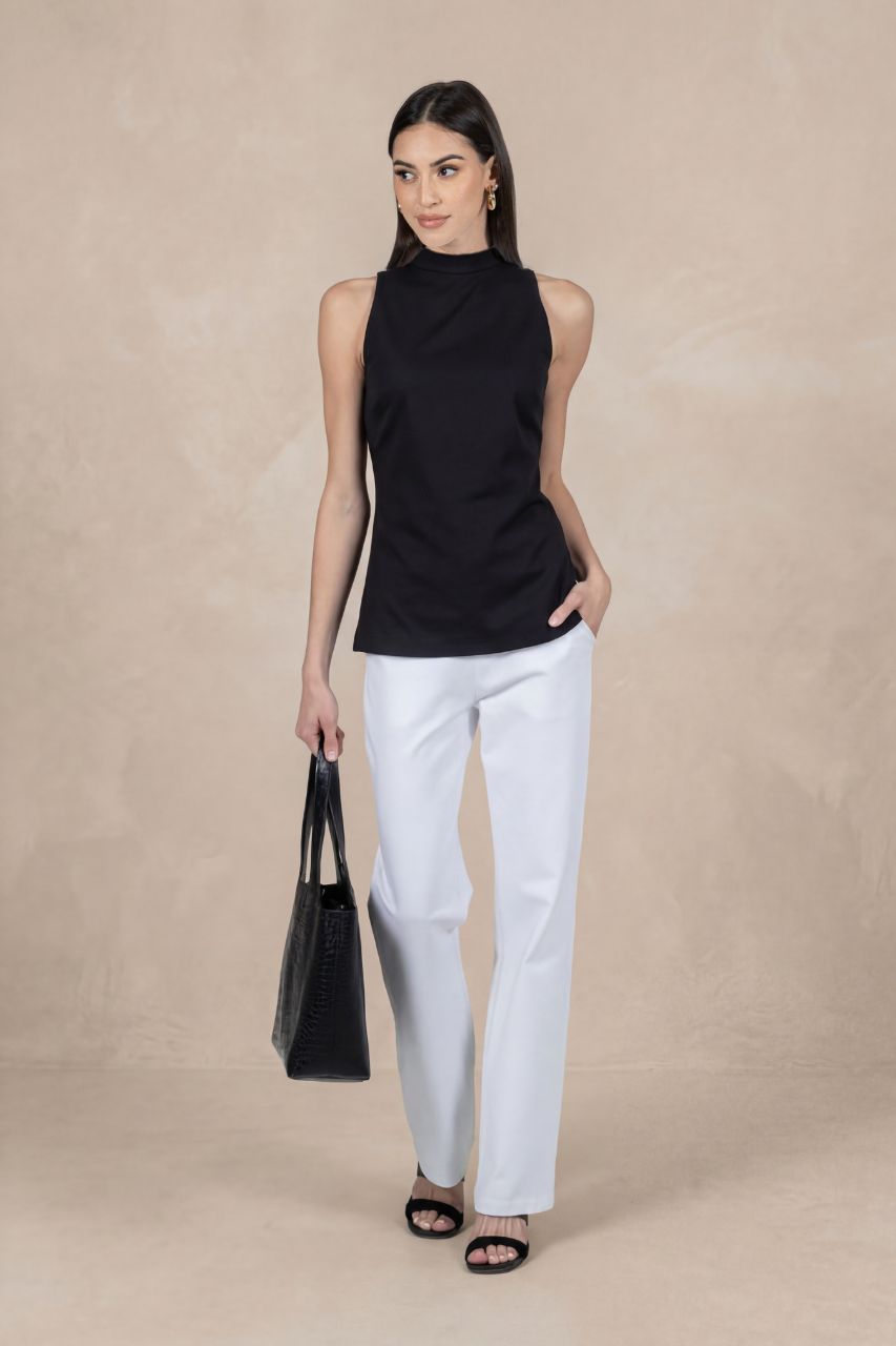 Woman wearing a black sleeveless top and white pants against a beige background