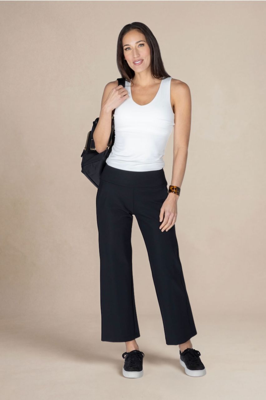 Woman wearing a white tank top and black cropped pants against a beige background