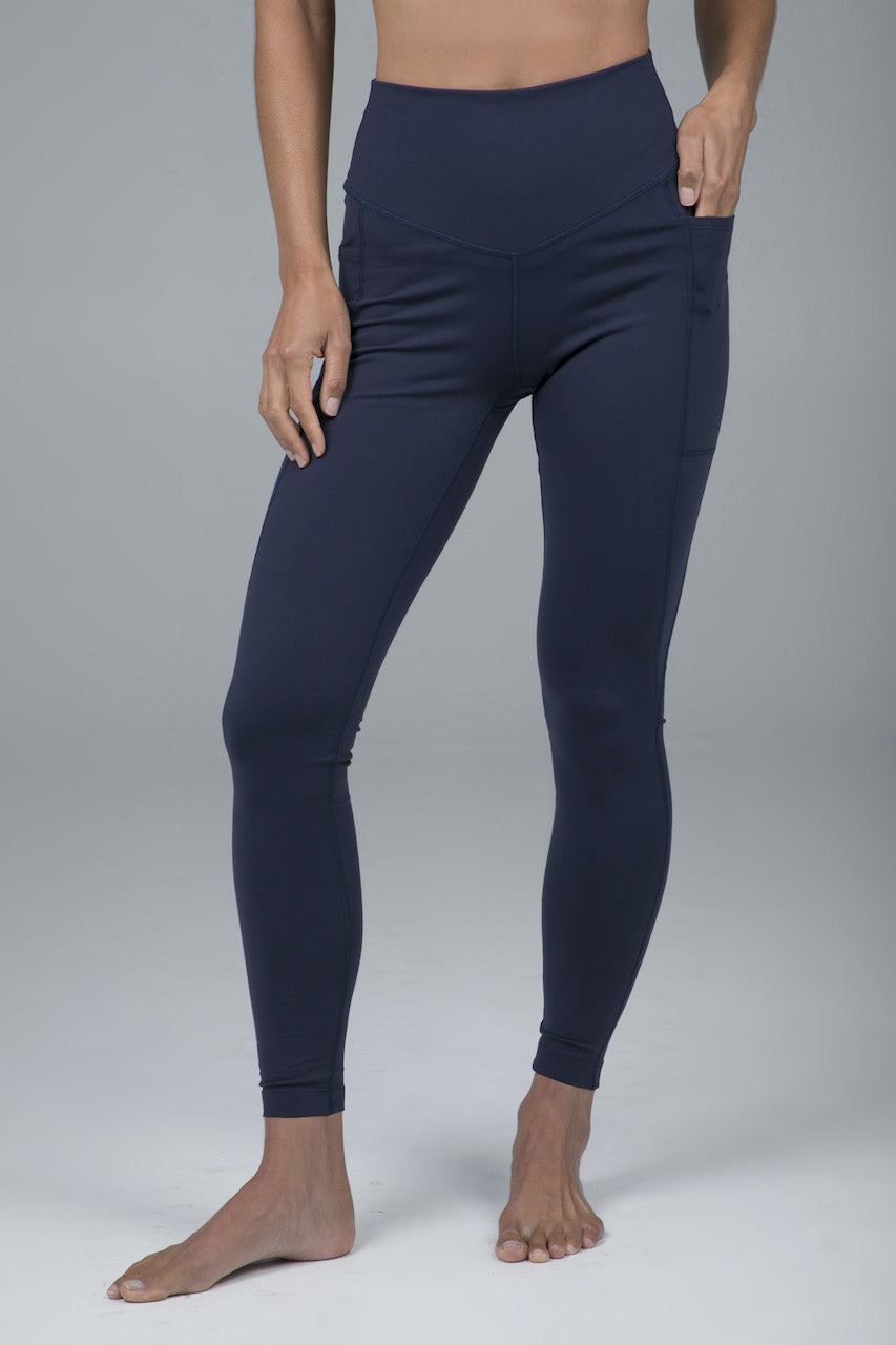 Front view of model wearing high waisted navy blue leggings with one hand in the side pockets