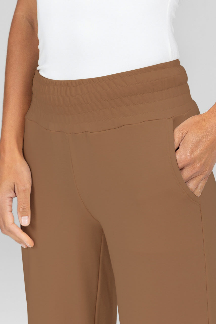 Close up photo of a model wearing light brown terry mid-rise sweatpants with a smocked waistband and front pockets