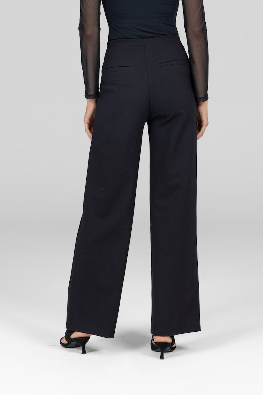 A model waist down facing away from the camera wearing high waisted black pants with a wide leg and pockets on the back.