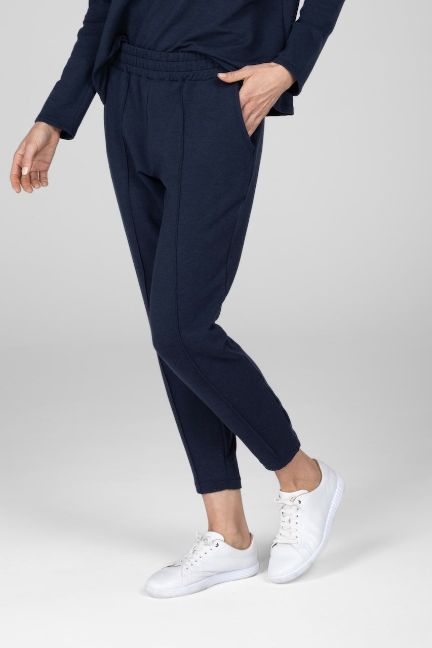 A woman wearing navy pintuck joggers and white sneakers standing with one hand in a pocket.