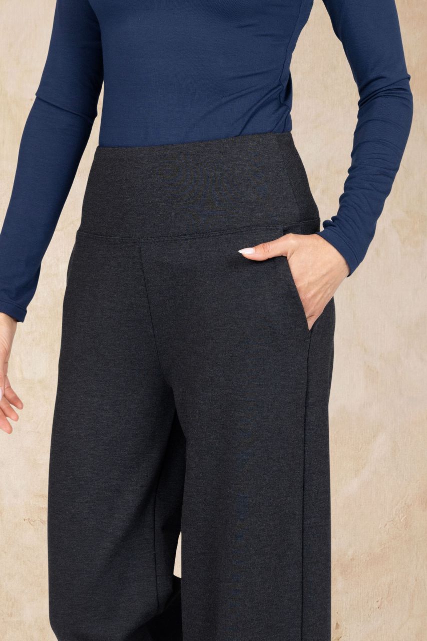 Person wearing a navy long-sleeve top and dark gray wide-leg pants against a beige background