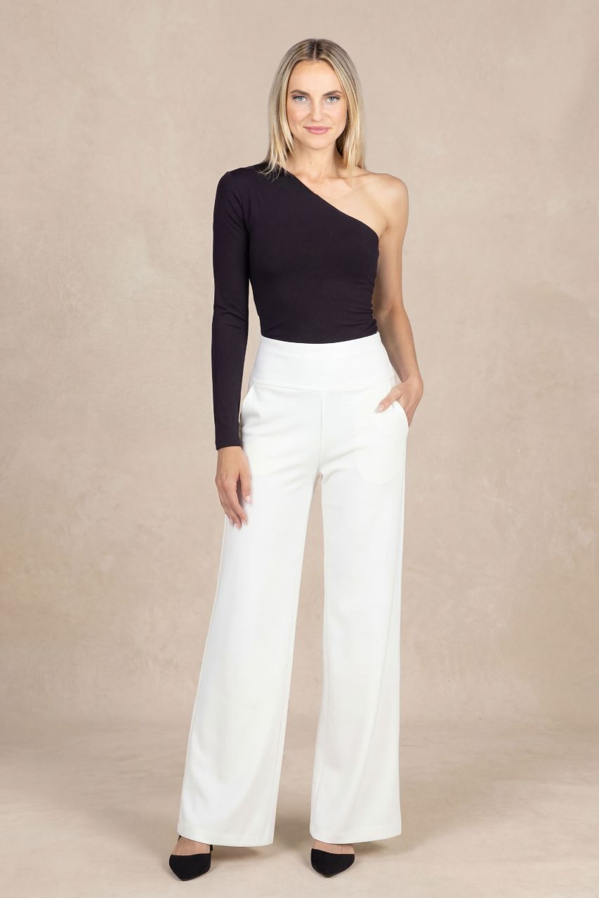 Woman wearing a black one-shoulder top and white pants against a beige background