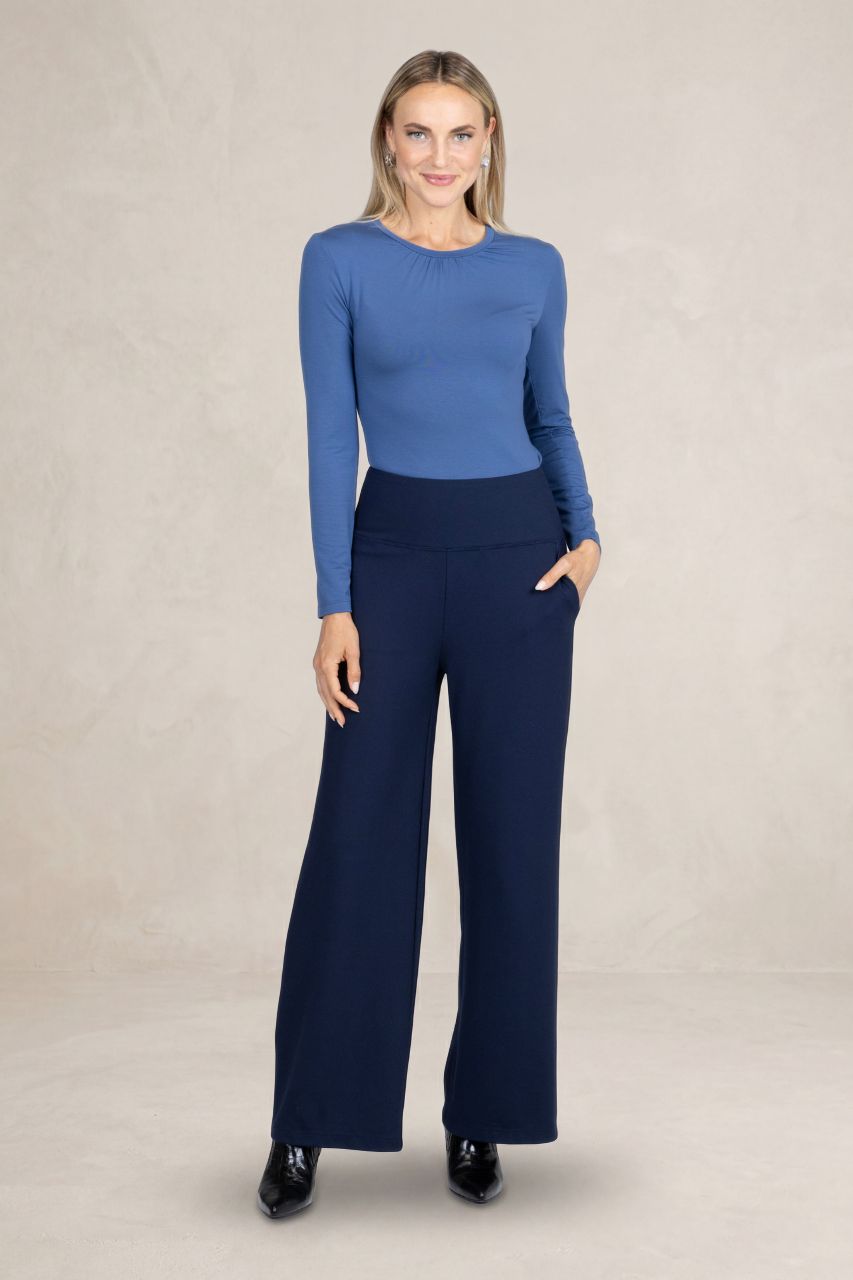 Woman wearing a blue top and navy pants on a beige background