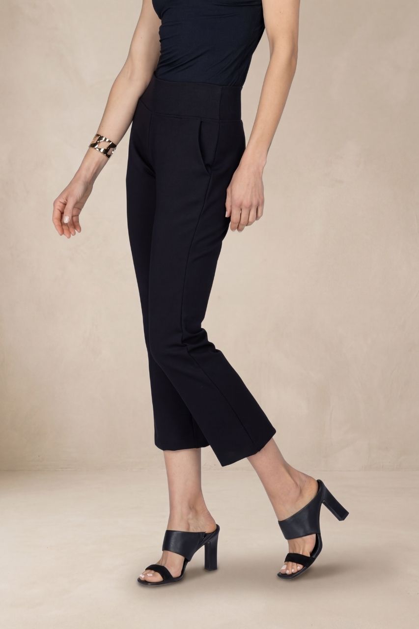 Person wearing black ankle pants and high-heeled shoes on a beige background