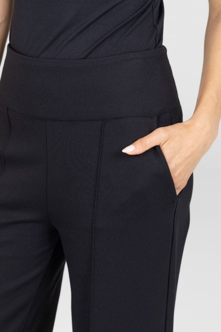 Close up view of black high-waisted pants worn by a woman on a light gray background