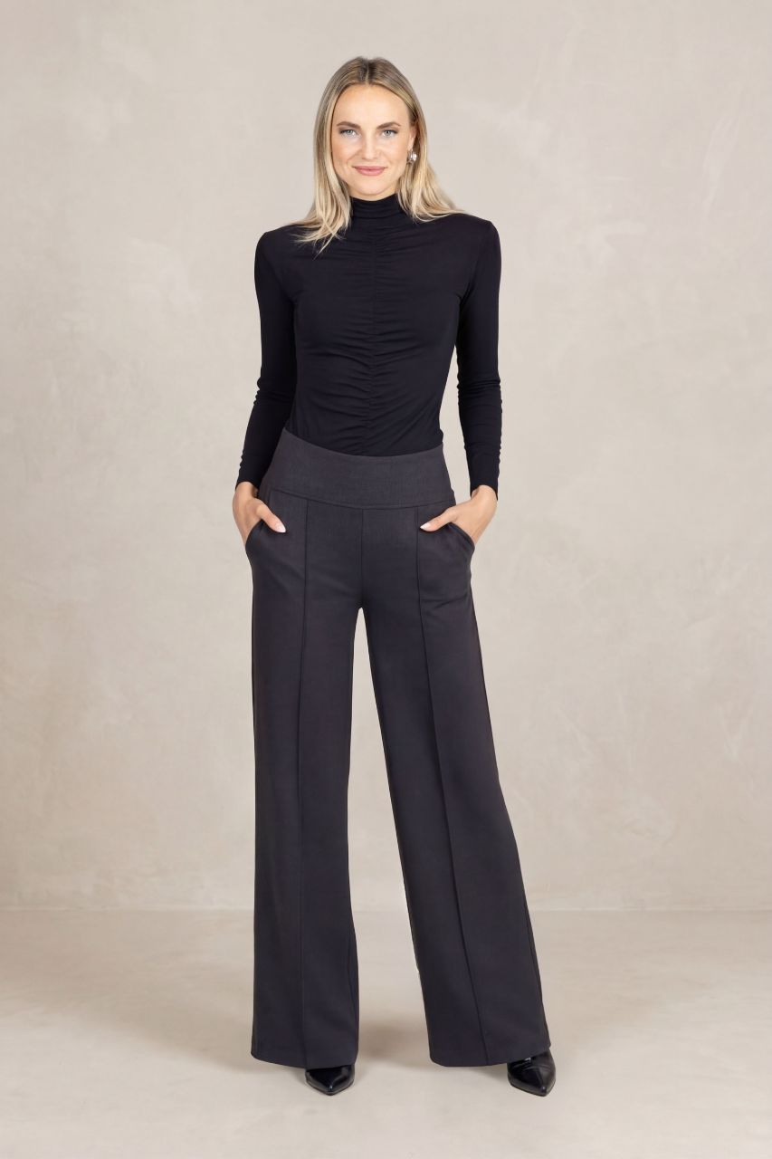 Woman wearing a black turtleneck and dark gray wide-leg pants on a beige background