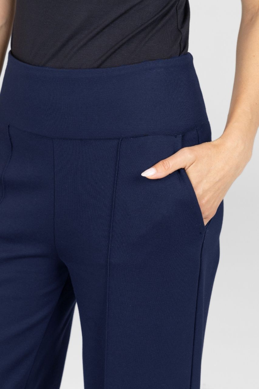 Close up view of navy blue pants worn by a woman on a light gray background