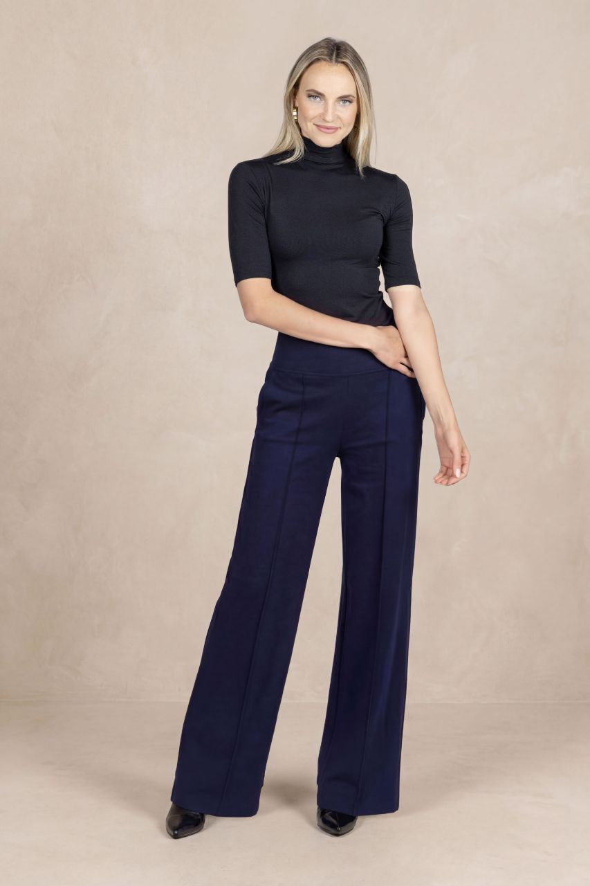 Woman wearing a black short sleeve mock neck and navy wide-leg pants against a beige background
