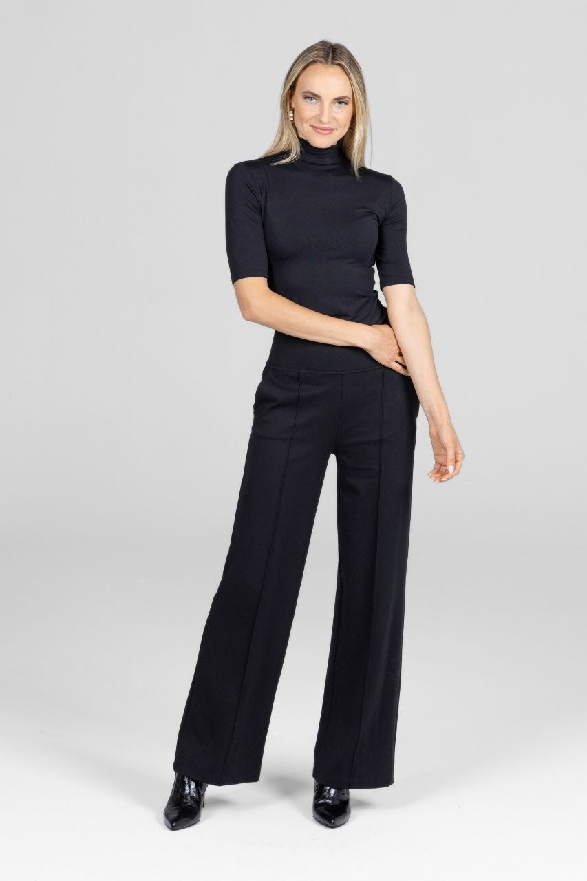 Woman wearing a black mockneck top and black wide-leg pants on a white background