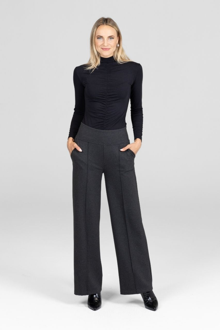 Woman wearing a black mock neck long sleeve top and gray high waisted wide leg pants on a white background