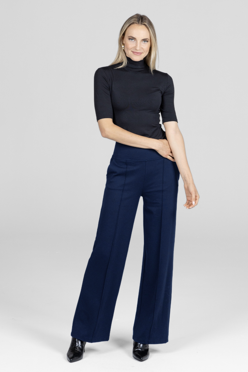 Woman wearing a black short sleeve mock neck tucked into navy wide-leg pants on a white background