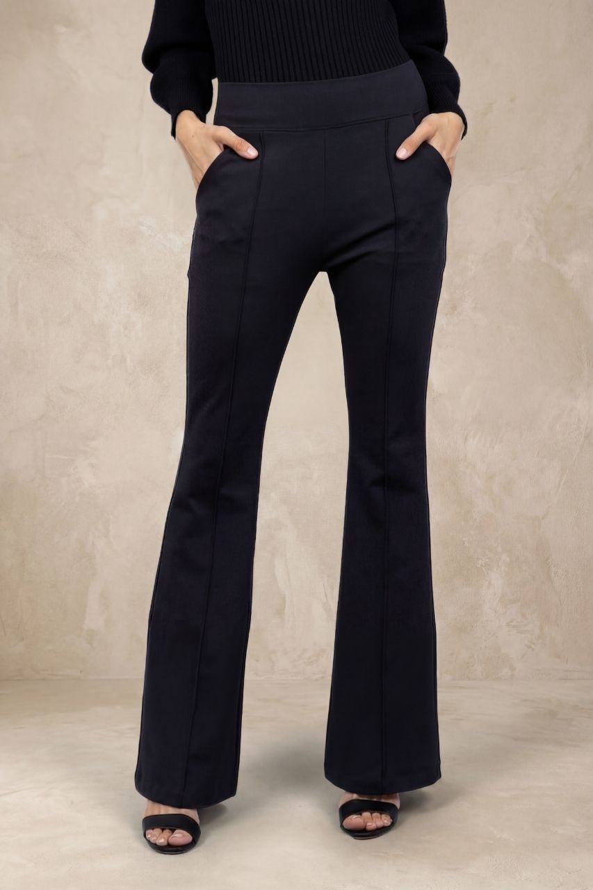 Woman wearing black flared pants with pintucks in front of a beige background