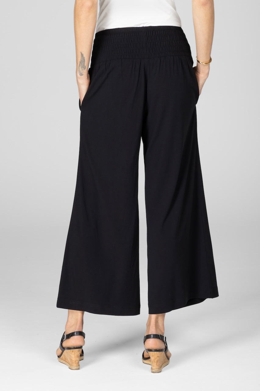 Back view of woman wearing black ankle pants with high rise smocked waistband