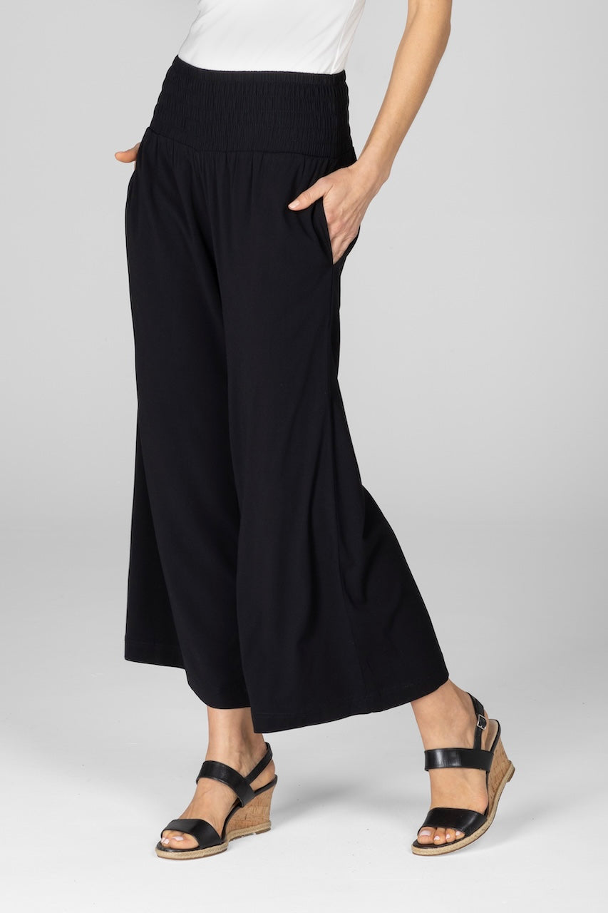 Woman wearing black high rise ankle pants with smocked waistband, side view