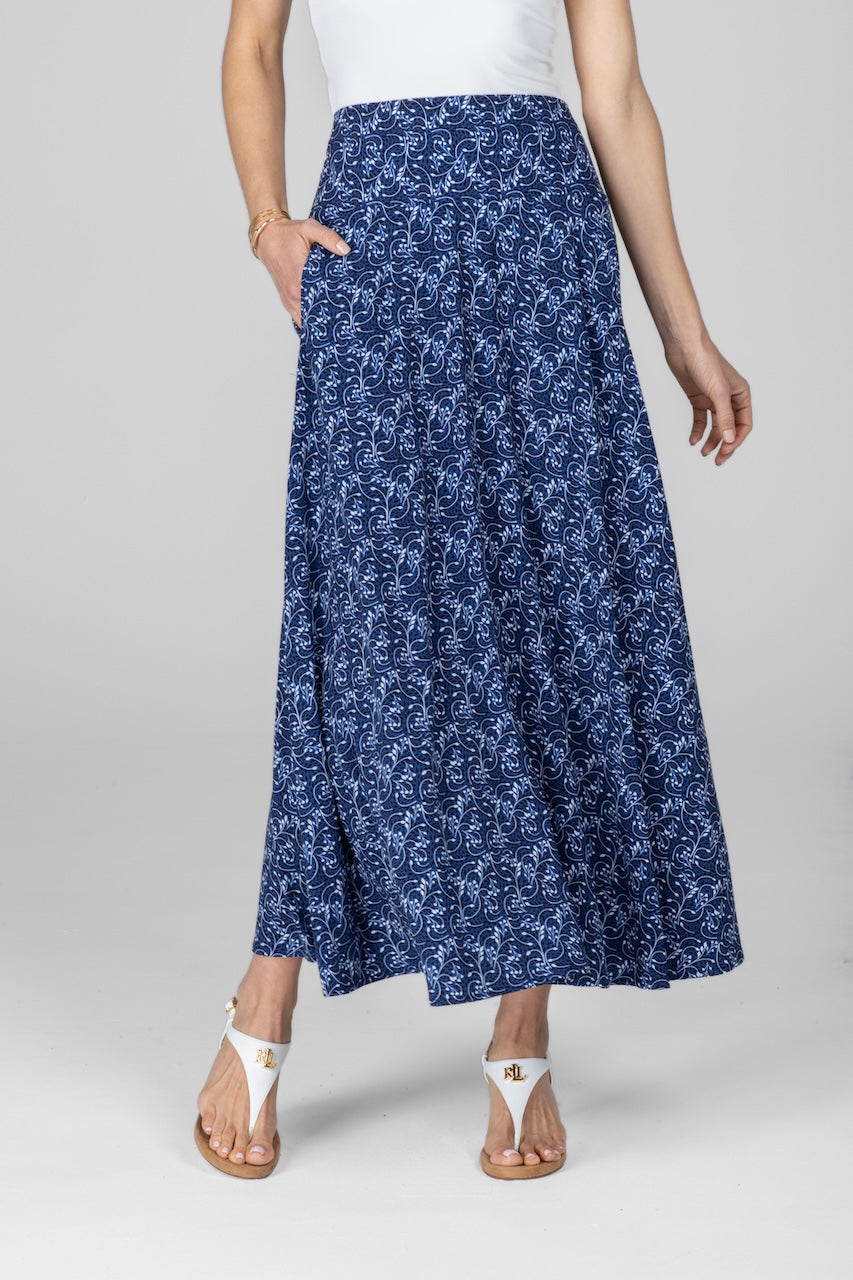 A woman wearing a blue floral maxi skirt with a A-line silhouette, paired with a white top and white sandals.
