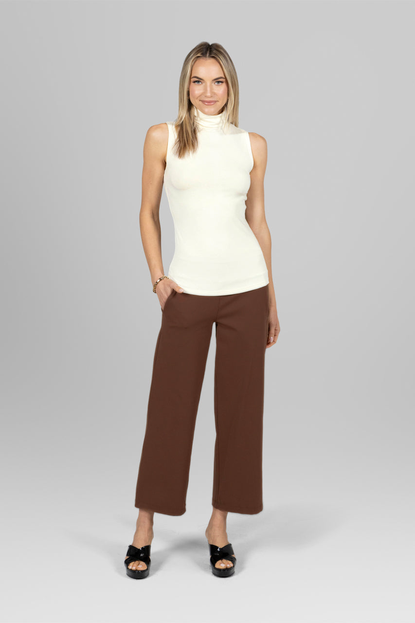 Woman wearing sleeveless turtleneck in ivory and brown ankle pants