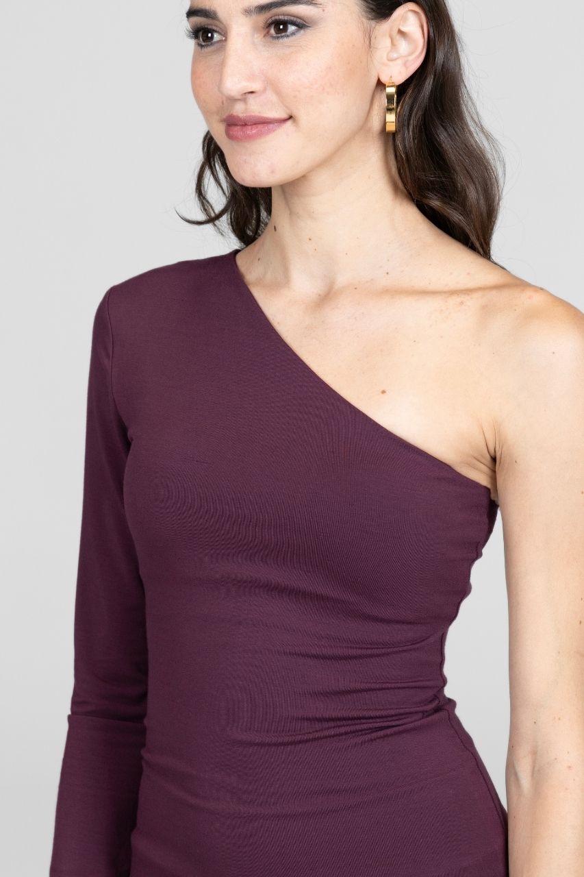Woman wearing a one-shoulder burgundy top against a plain background