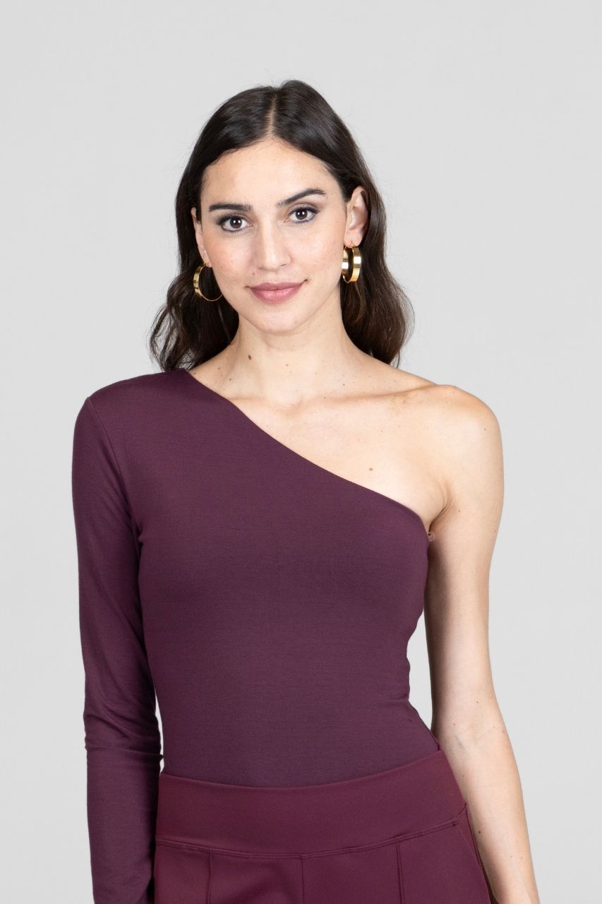 Woman wearing a one-shoulder burgundy top against a gray background