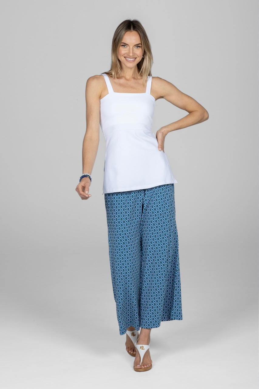 A woman wearing a white sleeveless top and blue pants with a geometric pattern.