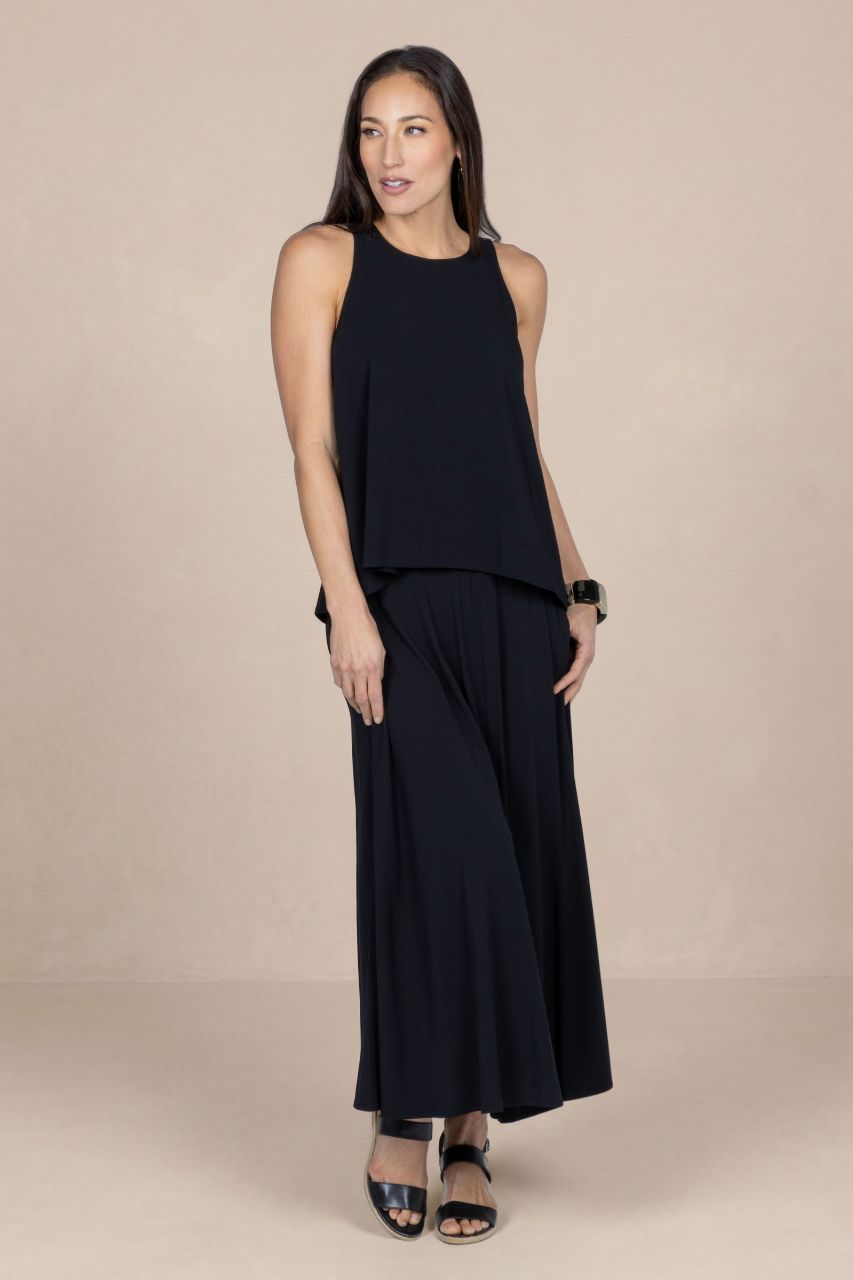 Woman wearing a black sleeveless top and maxi skirt on a beige background