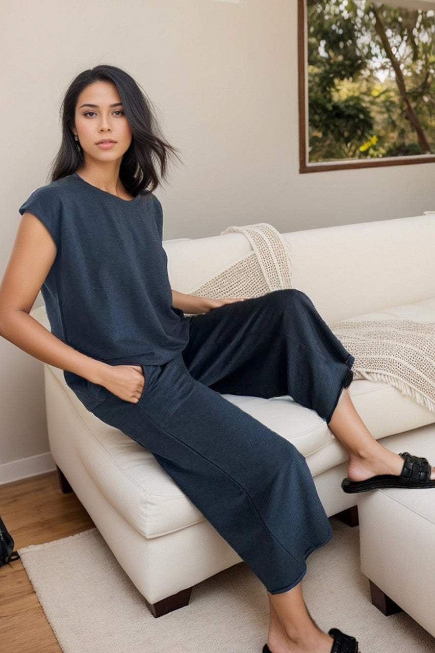 Woman wearing dark blue short sleeve top with matching cropped pants sitting on a couch