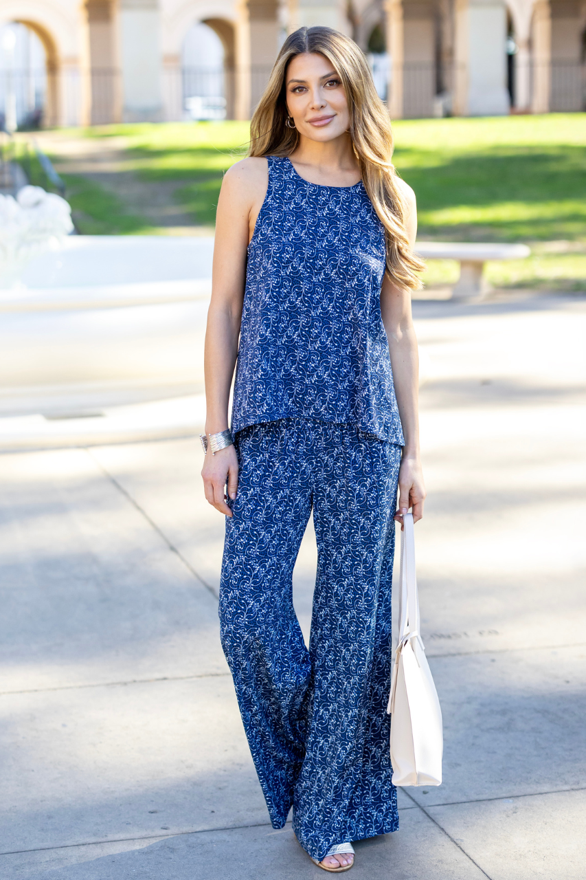 Woman wearing a sleeveless flowy top with blue vines print and matching pants