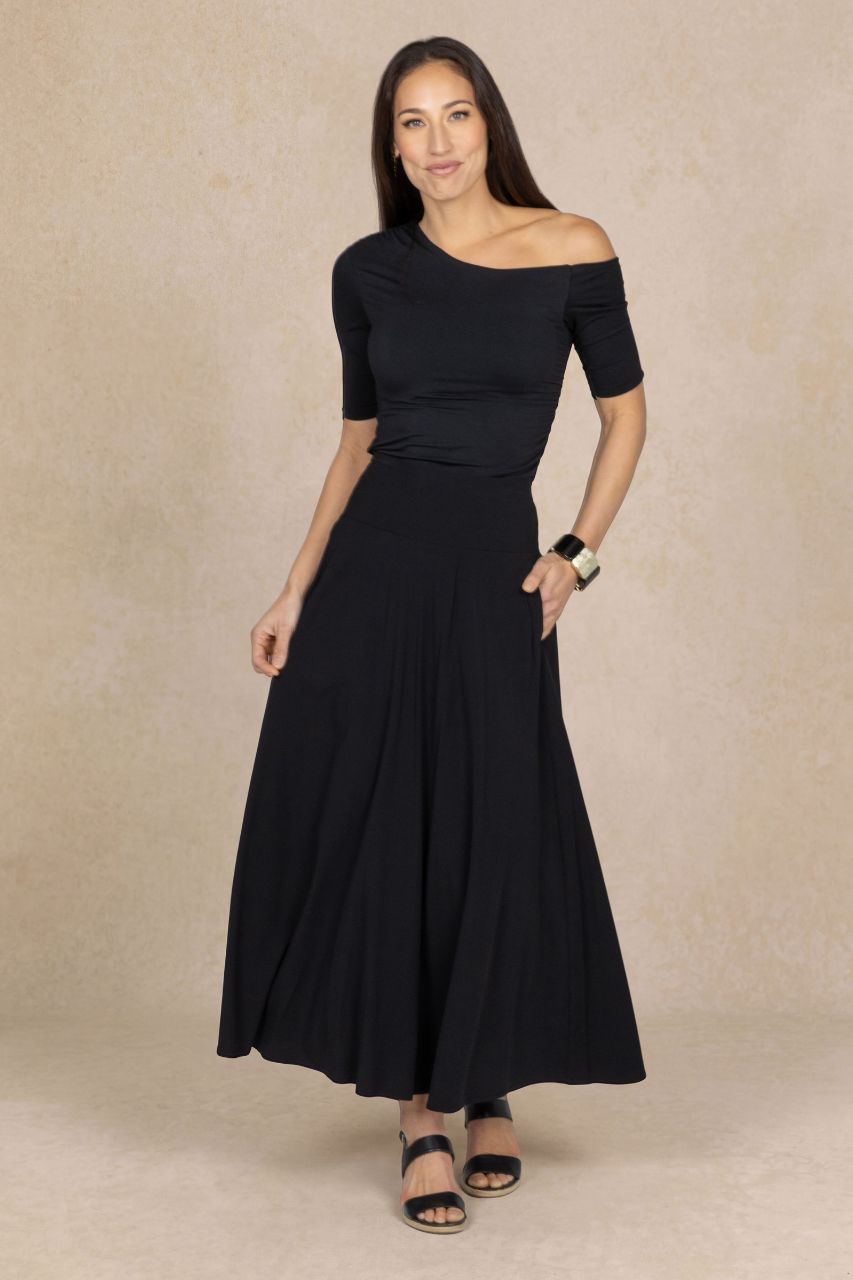 Full length image of a woman wearing a black off-shoulder top and a black maxi skirt on a beige background