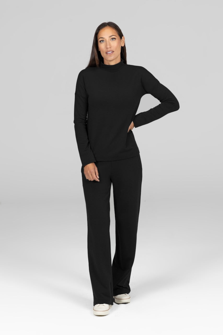 Model wearing black two piece matching set with a long sleeve mock neck and mid-waist wide leg french terry pants.