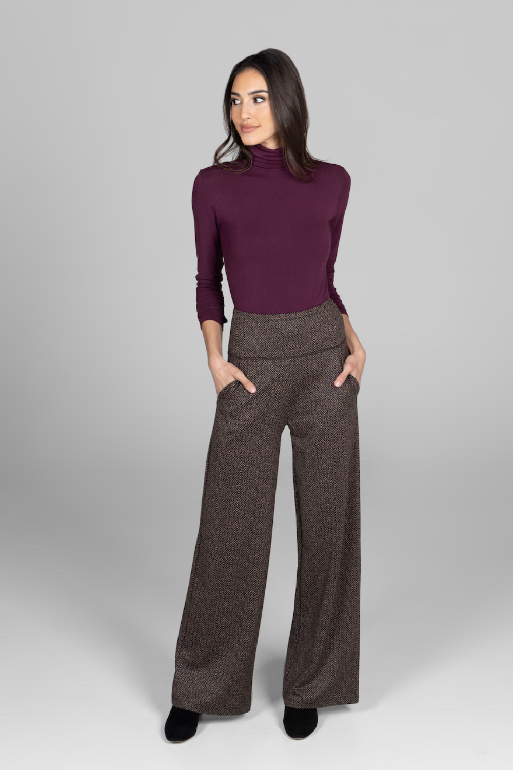 Woman wearing a burgundy long sleeve turtleneck and brown herringbone high waist wide-leg pants on a gray background