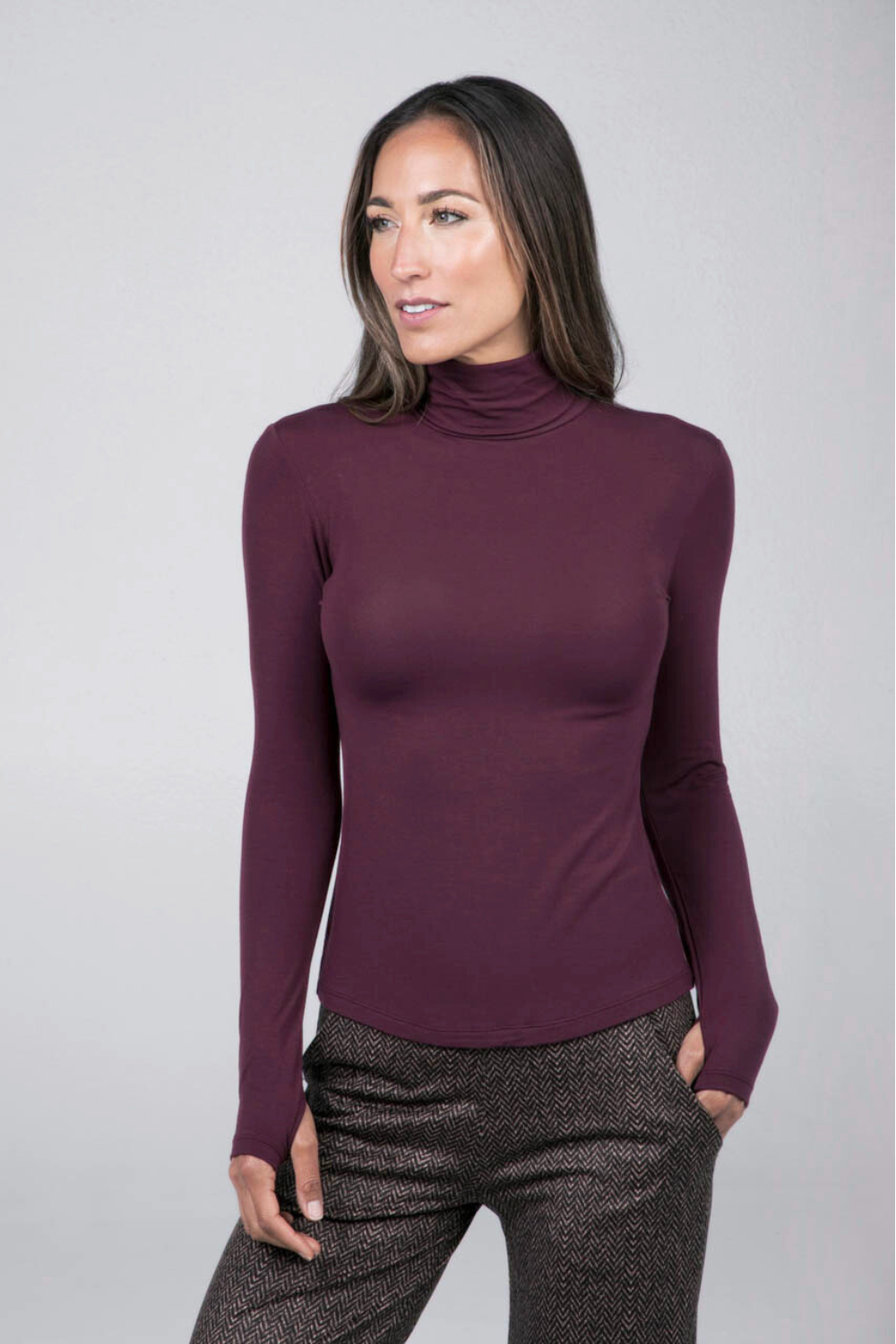 Woman wearing a burgundy turtleneck long sleeve top against a gray background